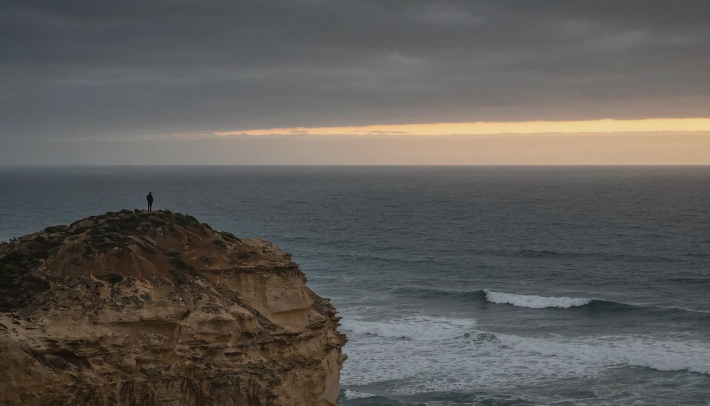 A lone figure on a sea cliff at dusk